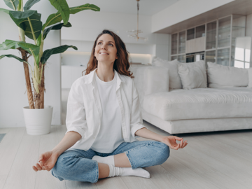 Corperformance - Tile Image - Serene lady sitting crossed legged with hands in meditation pose on the floor of a modern cream living room