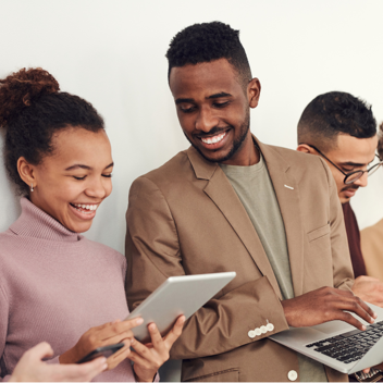 Lumina - Tile Image - A group of mixed race people dressed in neutral clothing smiling and looking at laptops and tablets